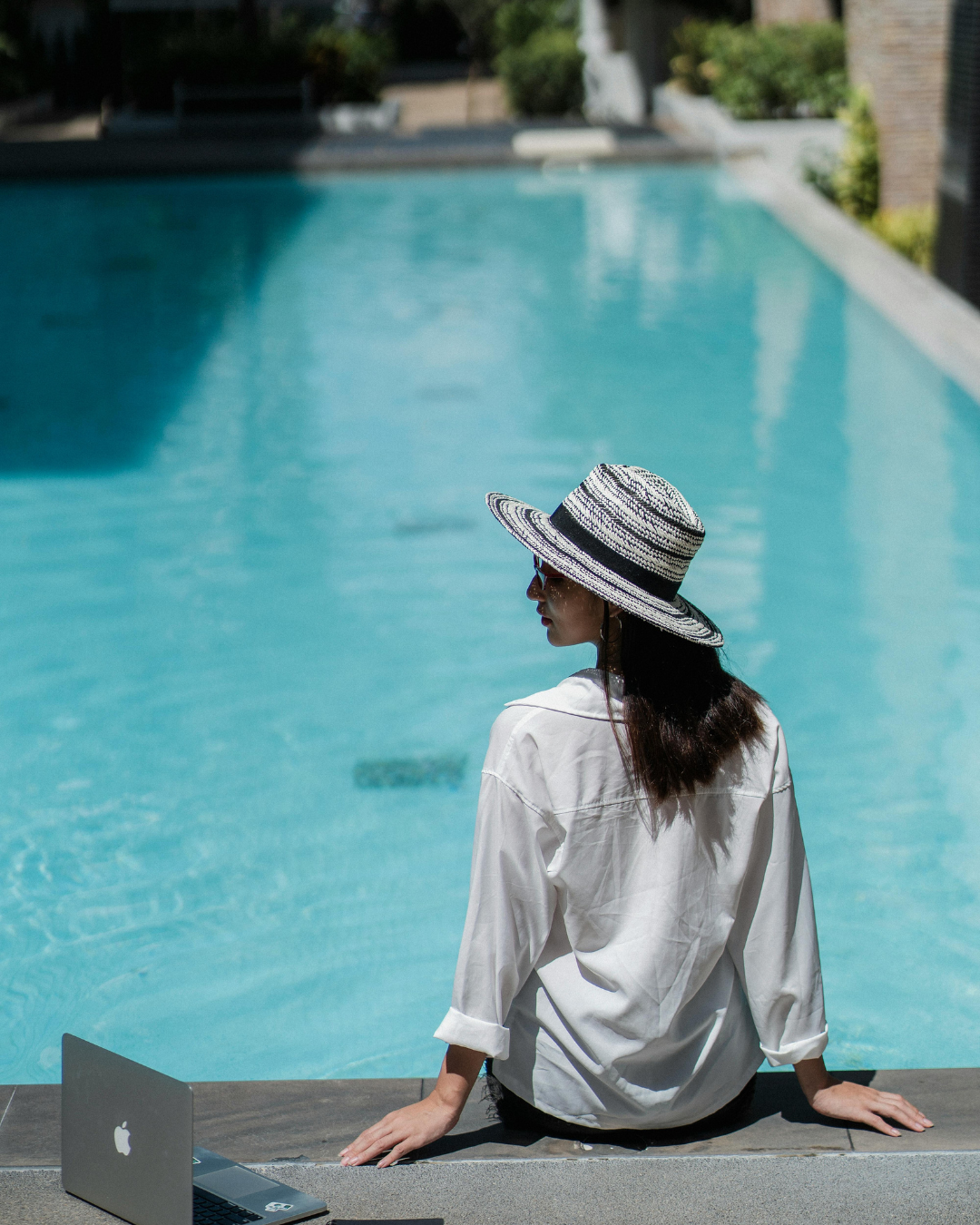 Woman sitting by pool with hat
